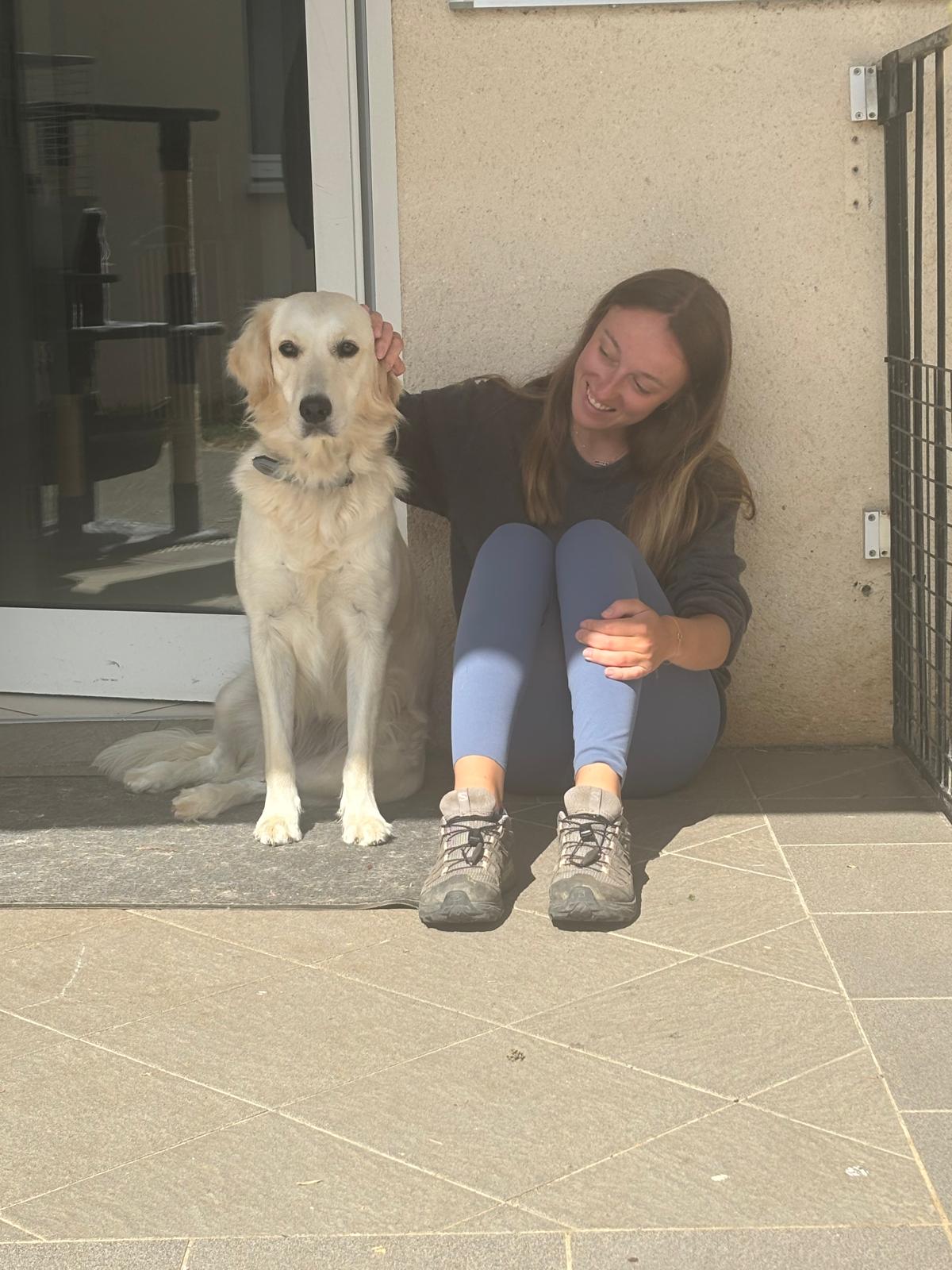 Marion assise au sol caressant un grand chien doré sur une terrasse